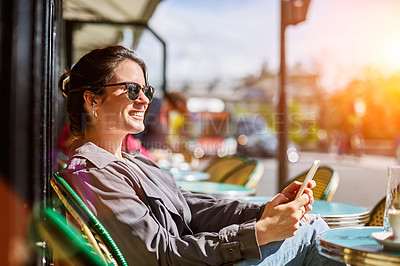 Buy stock photo Shot of a smiling young woman sitting at a sidewalk cafe in Paris using a digital tablet
