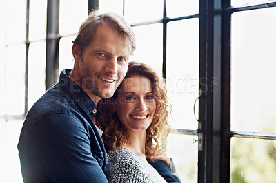 Buy stock photo Portrait of an affectionate mature couple hugging in front of a window at home