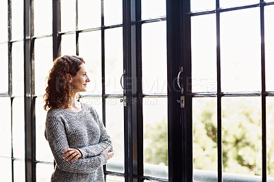 Buy stock photo Shot of a mature woman standing in her home looking through a window