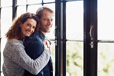 Buy stock photo Portrait of an affectionate mature couple hugging in front of a window at home