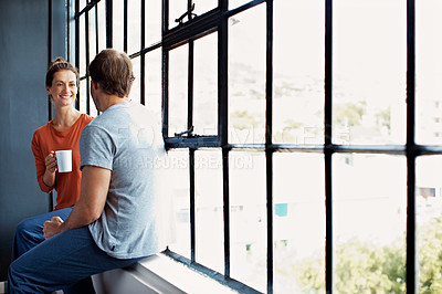Buy stock photo Shot of a happy mature couple sitting on a window sill at home drinking coffee and talking together