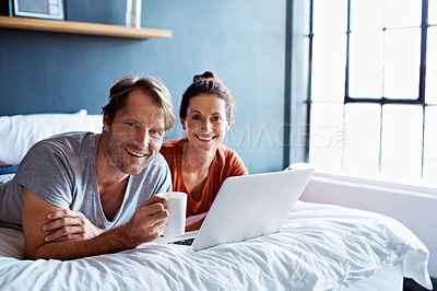 Buy stock photo Portrait of a smiling mature couple using a laptop and drinking coffee while lying on their bed
