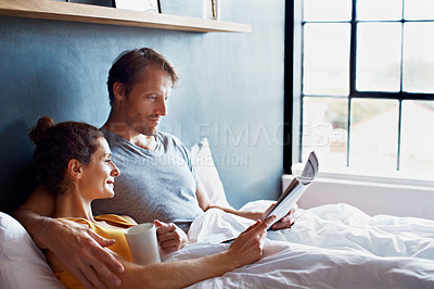 Buy stock photo Shot of a content mature couple reading the newspaper and drinking coffee while lying on their bed