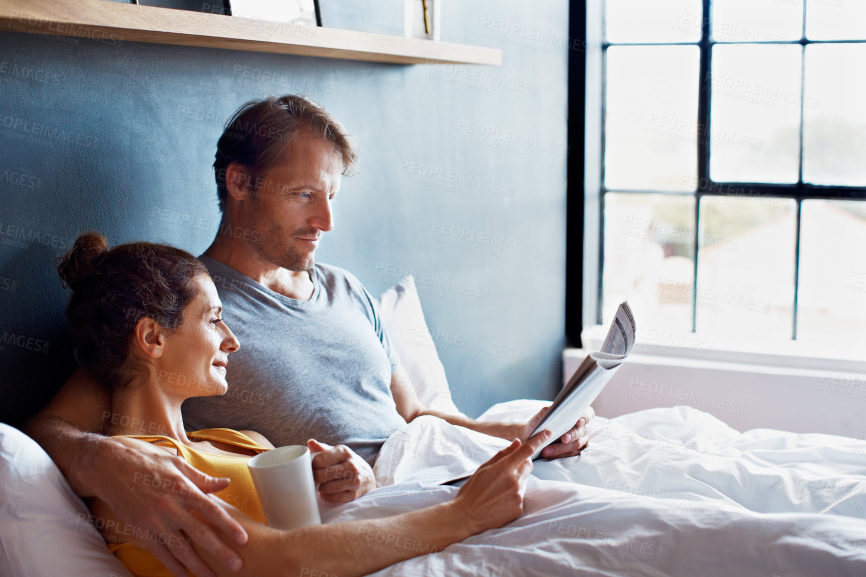 Buy stock photo Shot of a content mature couple reading the newspaper and drinking coffee while lying on their bed