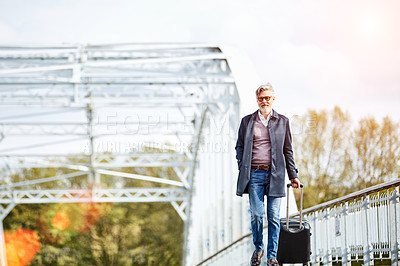 Buy stock photo Shot of a mature man pulling a suitcase while walking over a bridge in the city