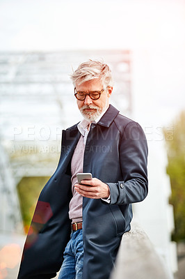 Buy stock photo Shot of a handsome mature man using a cellphone while standing on a bridge in the city