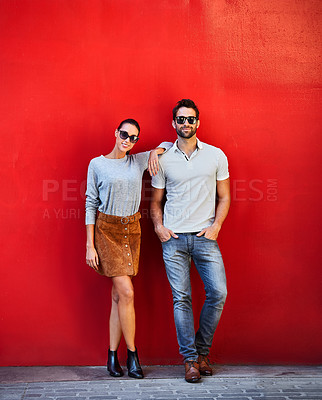 Buy stock photo Portrait of a stylish young couple leaning against a red wall outside