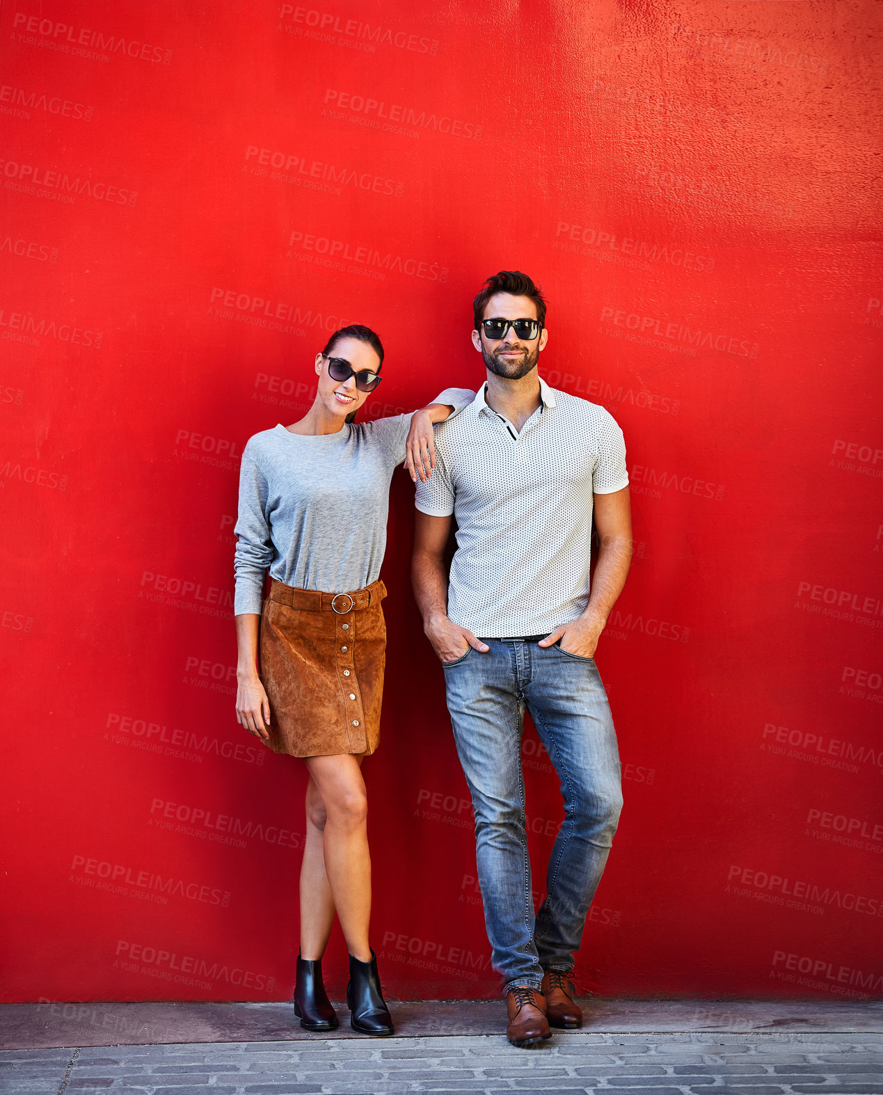 Buy stock photo Portrait of a stylish young couple leaning against a red wall outside