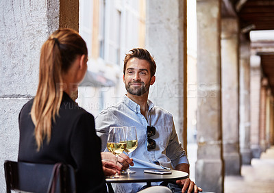 Buy stock photo Shot of a young couple sitting at a sidewalk table drinking wine and talking together