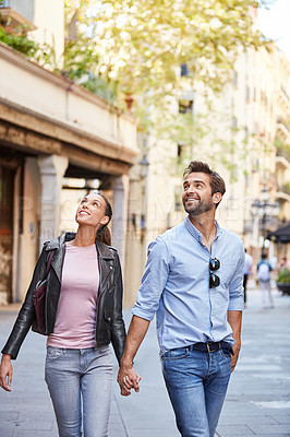 Buy stock photo Shot of an affectionate young couple walking hand in hand together in the city