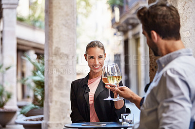 Buy stock photo Shot of a young couple sitting at a sidewalk table toasting with wine together