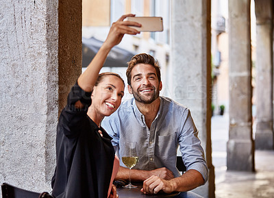 Buy stock photo Shot of a young couple sitting at a sidewalk table taking a selfie while drinking wine