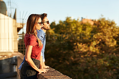 Buy stock photo Shot of a smiling young couple leaning on a balcony in the city looking at the view
