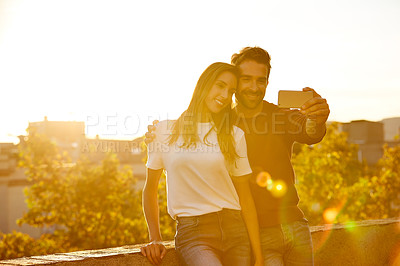 Buy stock photo Shot of a smiling couple taking a selfie together while standing on a balcony overlooking the city