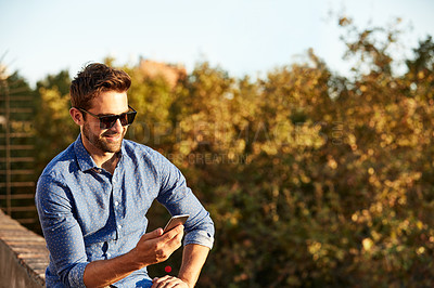 Buy stock photo Shot of a handsome young man sitting on a balcony using a cellphone
