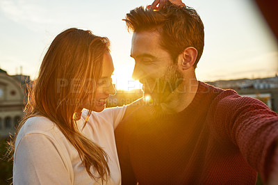 Buy stock photo Shot of a smiling couple taking a selfie together while standing on a balcony overlooking the city