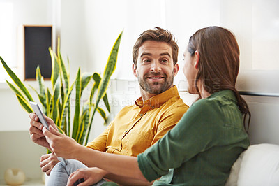 Buy stock photo Shot of a smiling young couple using a digital tablet together while relaxing in their living room