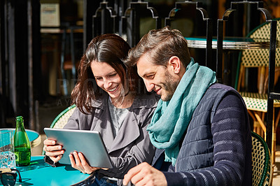 Buy stock photo Shot of a smiling couple sitting together at a table at a sidewalk cafe using a digital tablet
