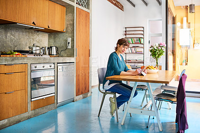 Buy stock photo Portrait of a young woman sitting at her kitchen table using a digital tablet