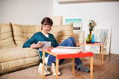Buy stock photo Shot of a young woman sitting on her living room floor using a digital tablet