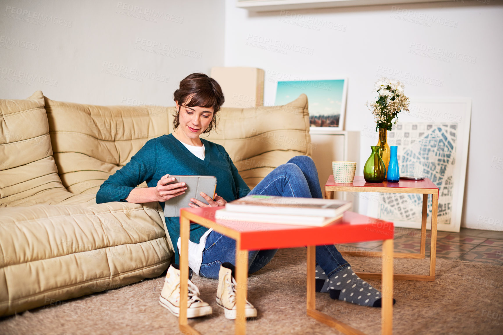 Buy stock photo Shot of a young woman sitting on her living room floor using a digital tablet