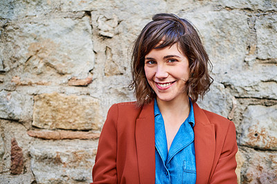 Buy stock photo Portrait of a smiling young woman standing outside in front of a stone wall