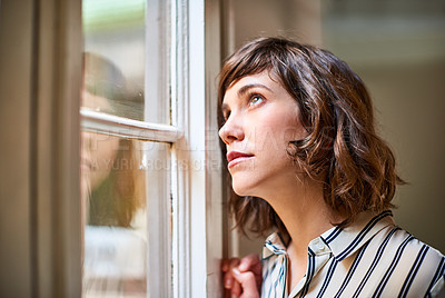 Buy stock photo Shot of a young woman looking up through a window at home