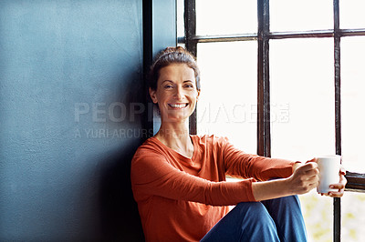 Buy stock photo Portrait of an attractive mature woman sitting on a window sill at home drinking a cup of coffee