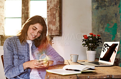 Buy stock photo Shot of a smiling young woman using a cellphone while sitting at a desk at home