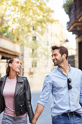 Buy stock photo Portrait of an affectionate young couple walking hand in hand together in the city
