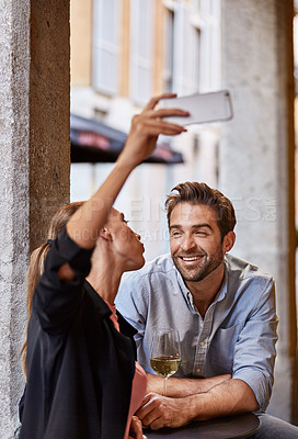 Buy stock photo Shot of a young couple sitting at a sidewalk table taking a selfie while drinking wine