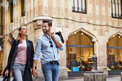 Buy stock photo Shot of an affectionate young couple walking hand in hand together in the city