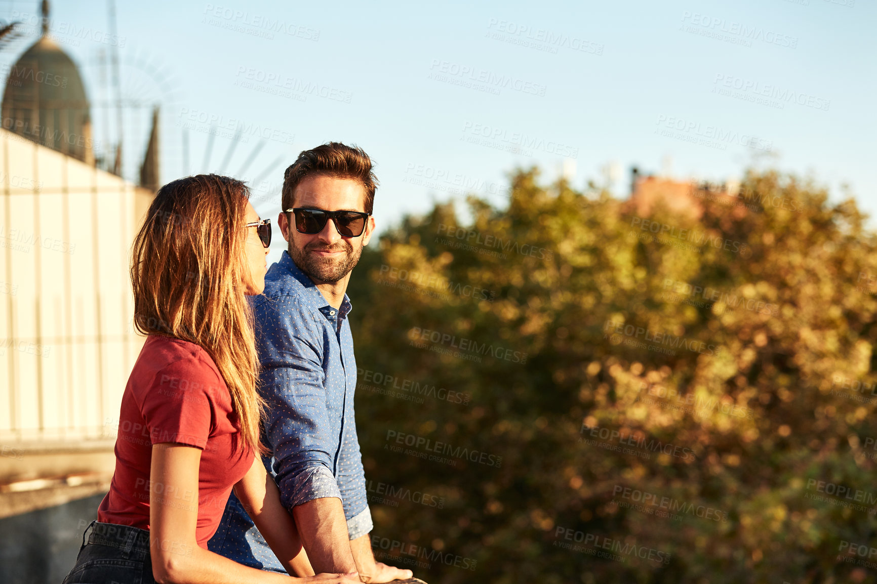 Buy stock photo Shot of a smiling young couple talking together while leaning on a balcony in the city looking at the view