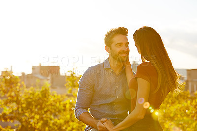 Buy stock photo Shot of a affectionate young couple sitting on a rooftop together at sunset