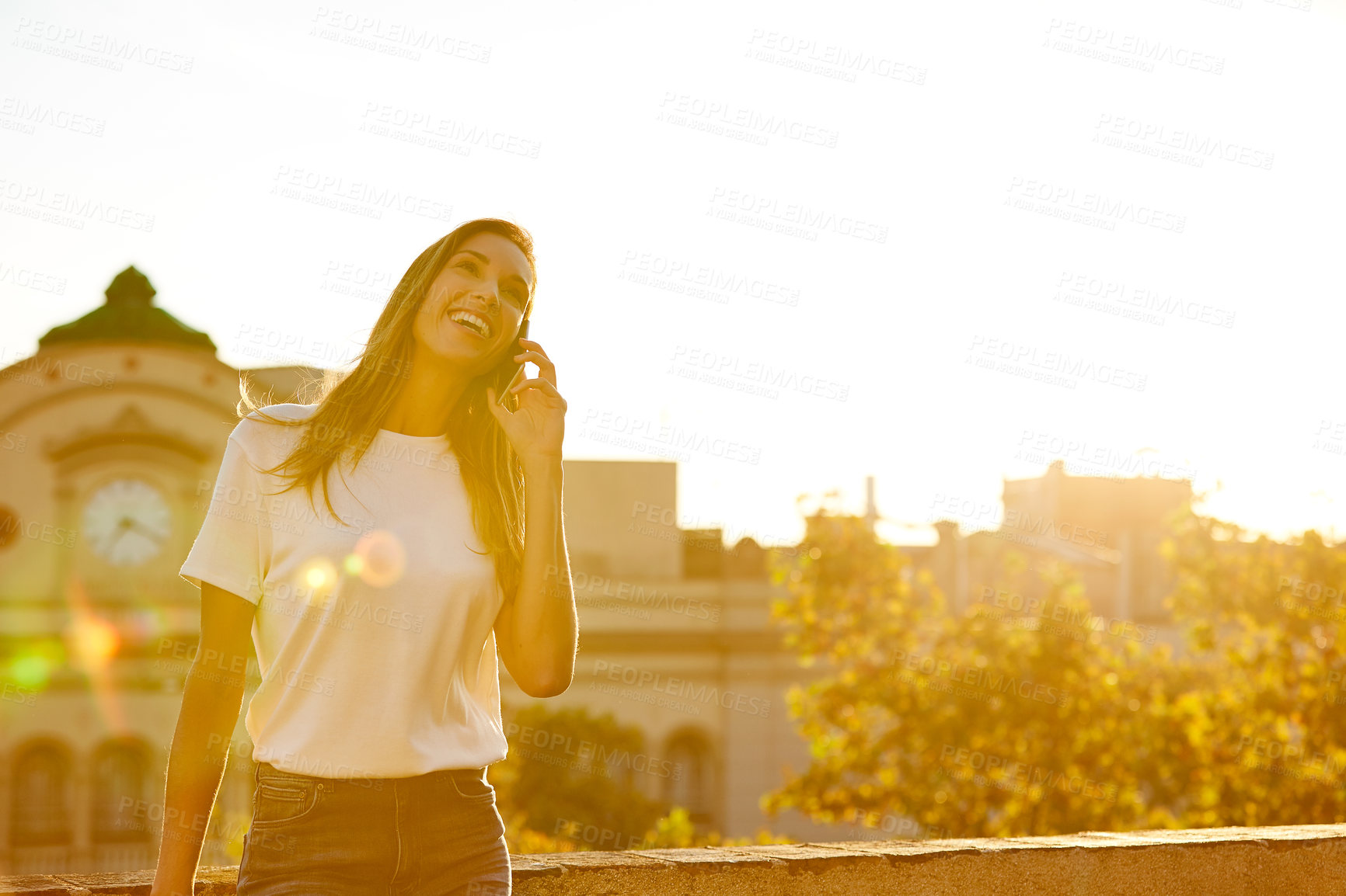 Buy stock photo Shot of an attractive young woman leaning on a wall on a cellphone with the city in the background