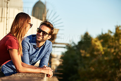 Buy stock photo Shot of a smiling young couple talking together while leaning on a balcony in the city looking at the view
