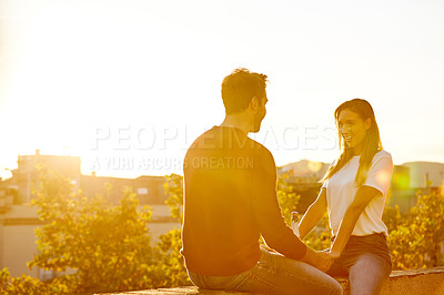 Buy stock photo Shot of a affectionate young couple sitting on a rooftop together at sunset