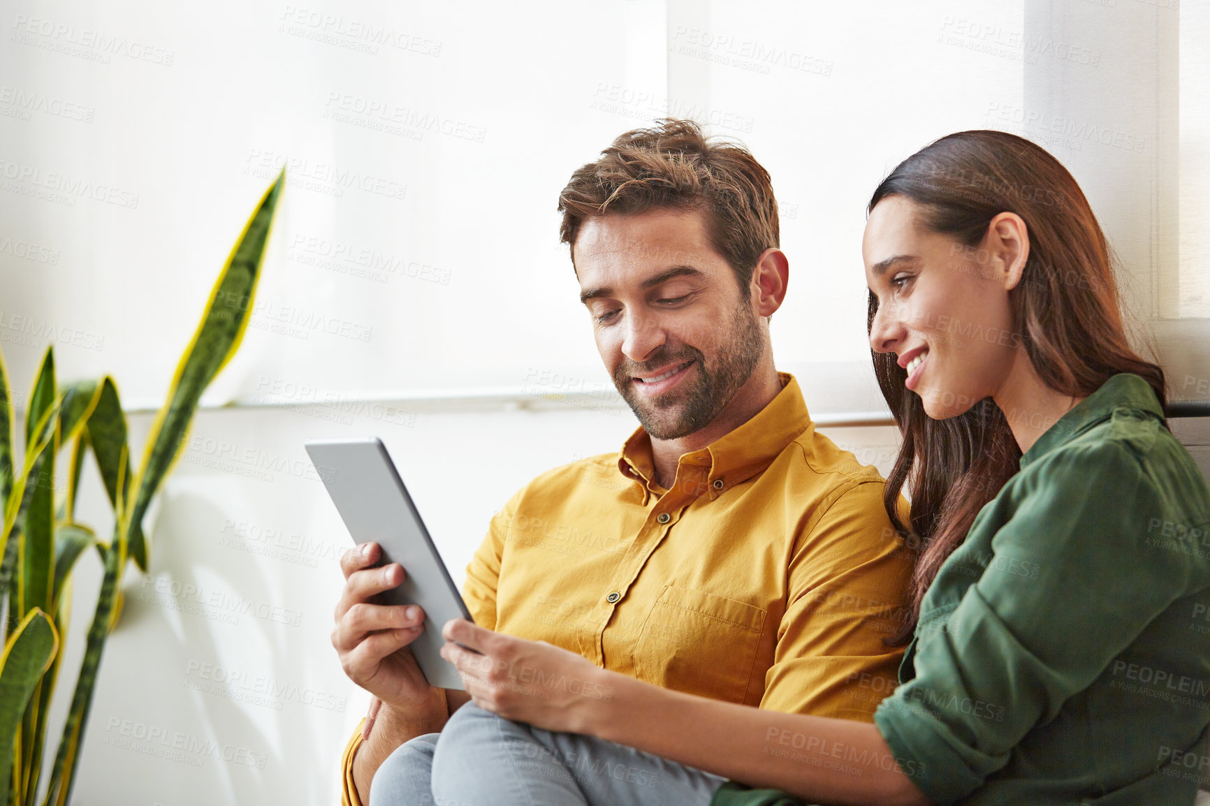 Buy stock photo Shot of a smiling young couple using a digital tablet together while relaxing in their living room