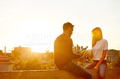 Buy stock photo Shot of a smiling couple drinking champagne while sitting on their rooftop at sunset