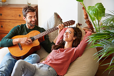 Buy stock photo Shot of a young man playing guitar for his girlfriend while relaxing in their living room