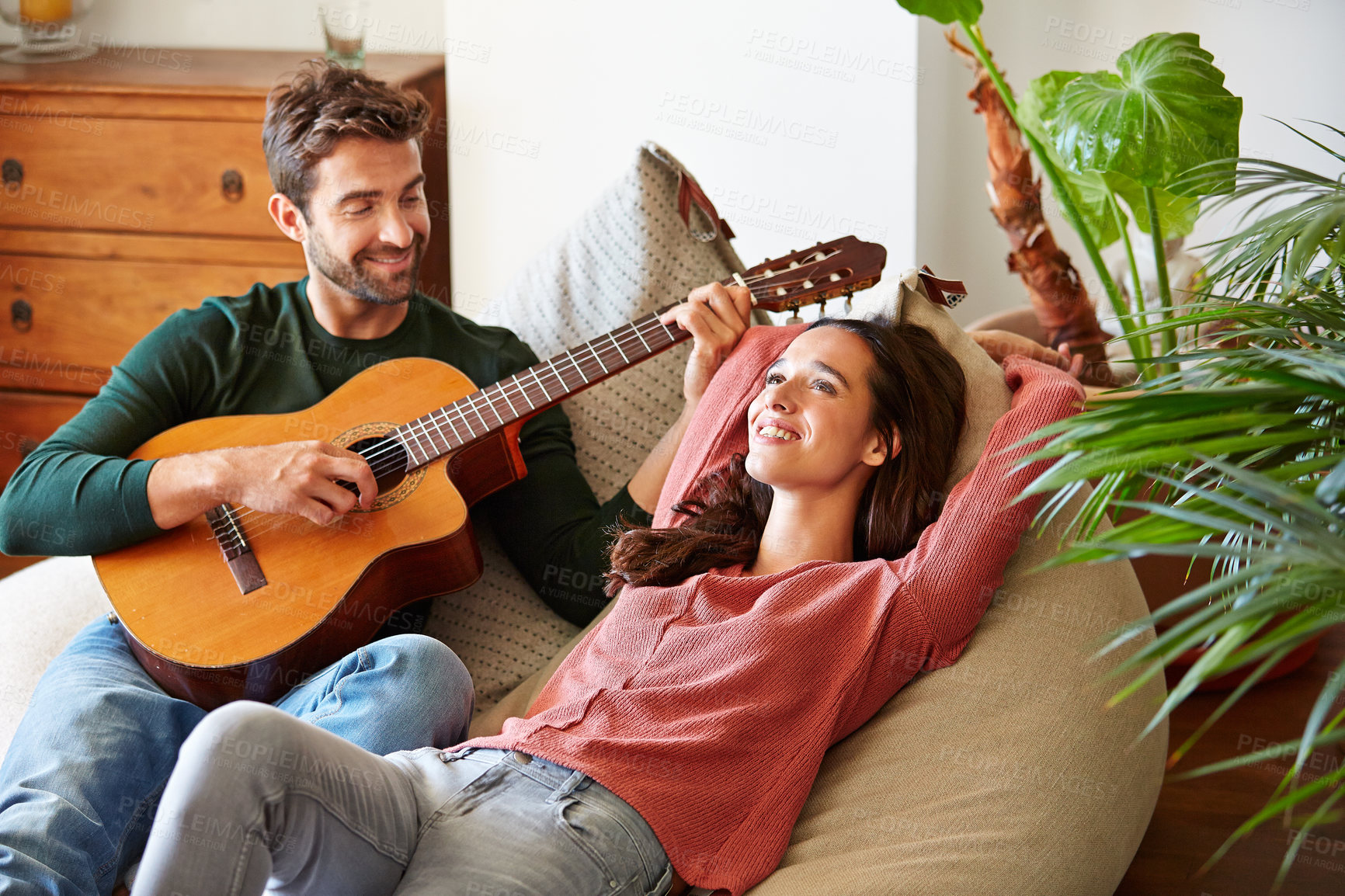 Buy stock photo Shot of a young man playing guitar for his girlfriend while relaxing in their living room