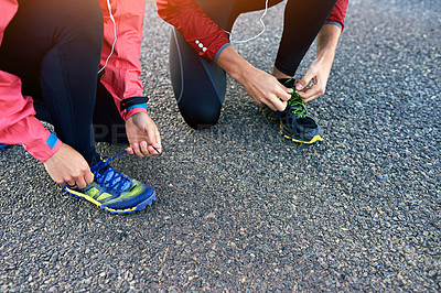Buy stock photo Cropped shot of two friends tying up their running shoes while out for a jog