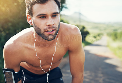Buy stock photo Shot of a focused young man listening to music on headphones before going for a run