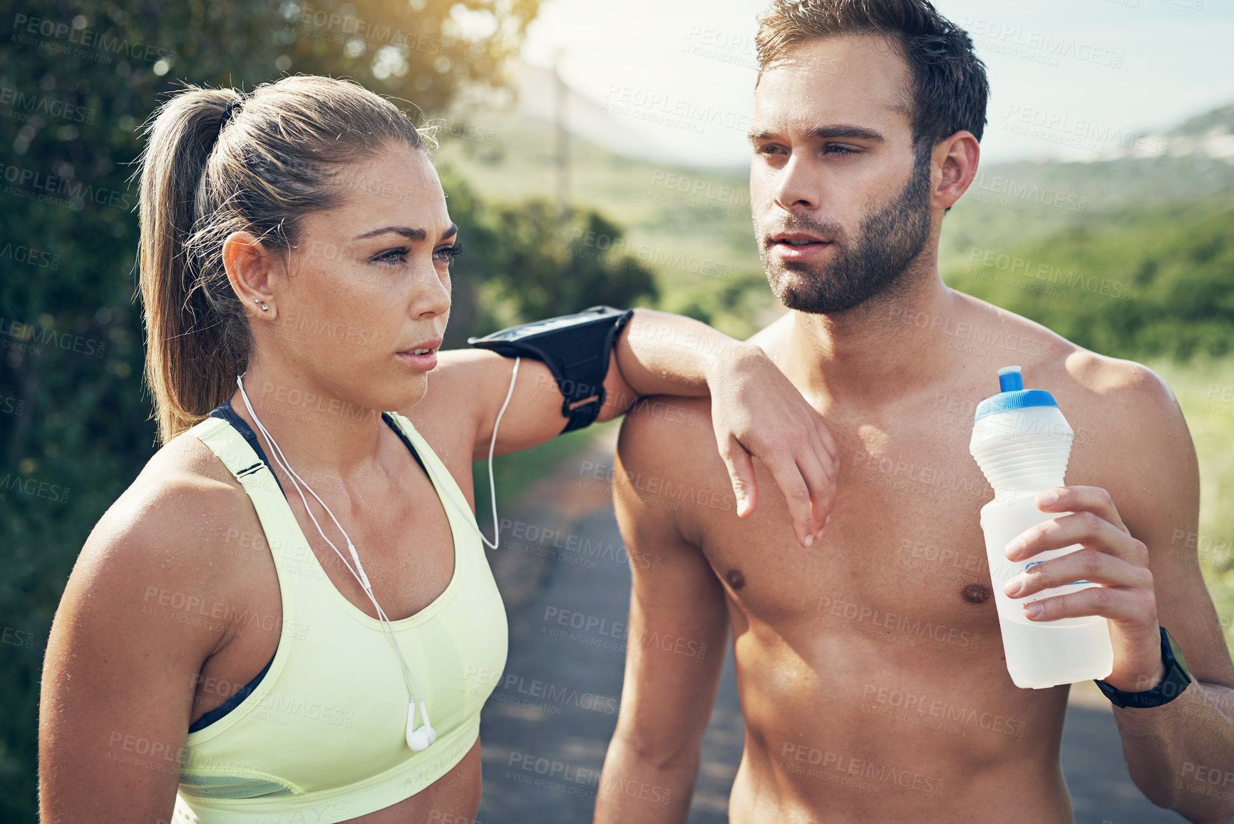 Buy stock photo Shot of two young friends drinking water while taking a break from an early morning run