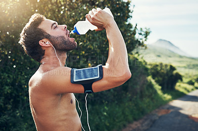 Buy stock photo Shot of a young man drinking from a water bottle while taking a break from an early morning run