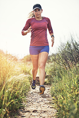 Buy stock photo Shot of a focused young woman running alone outside on a trail