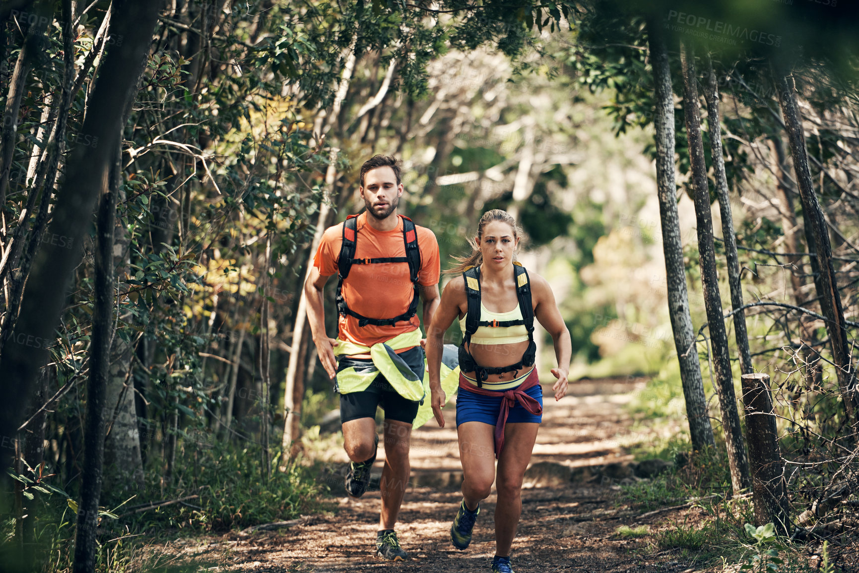 Buy stock photo Shot of two young friends running together along a trail in a forest