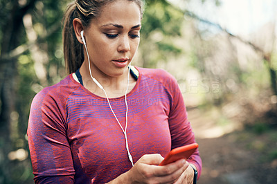 Buy stock photo Shot of a young woman listening to music on an mp3 player while out for a run in the forest