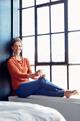 Buy stock photo Portrait of an attractive mature woman sitting on a window sill at home drinking a cup of coffee