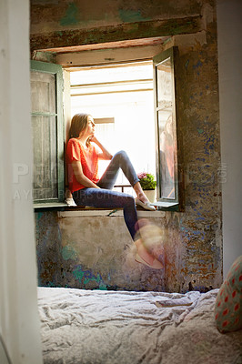 Buy stock photo Shot of an attractive young woman sitting on a window sill at home